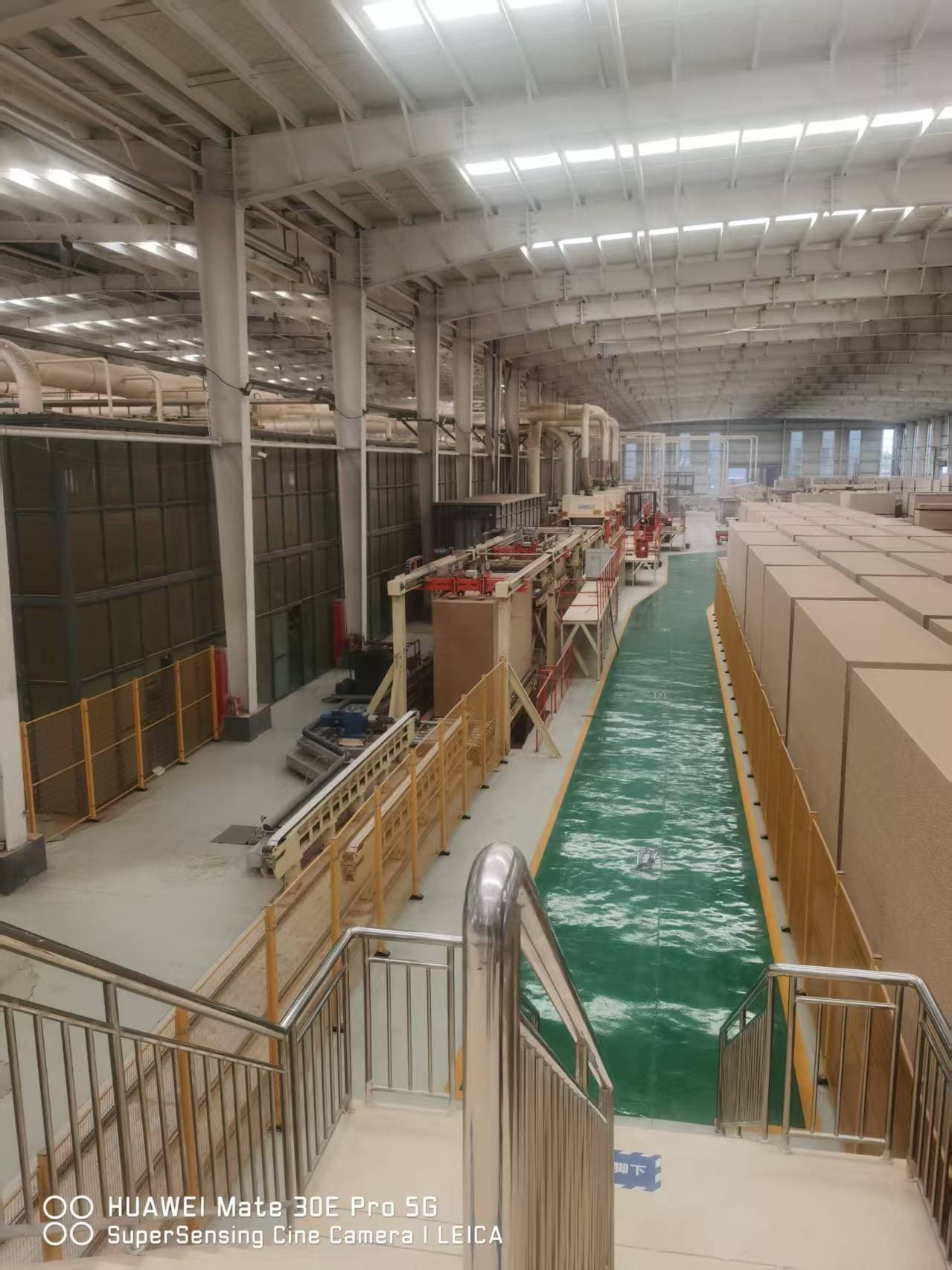 Workshop aisle beside board-handling equipment and stacked panels at CUZI MDF